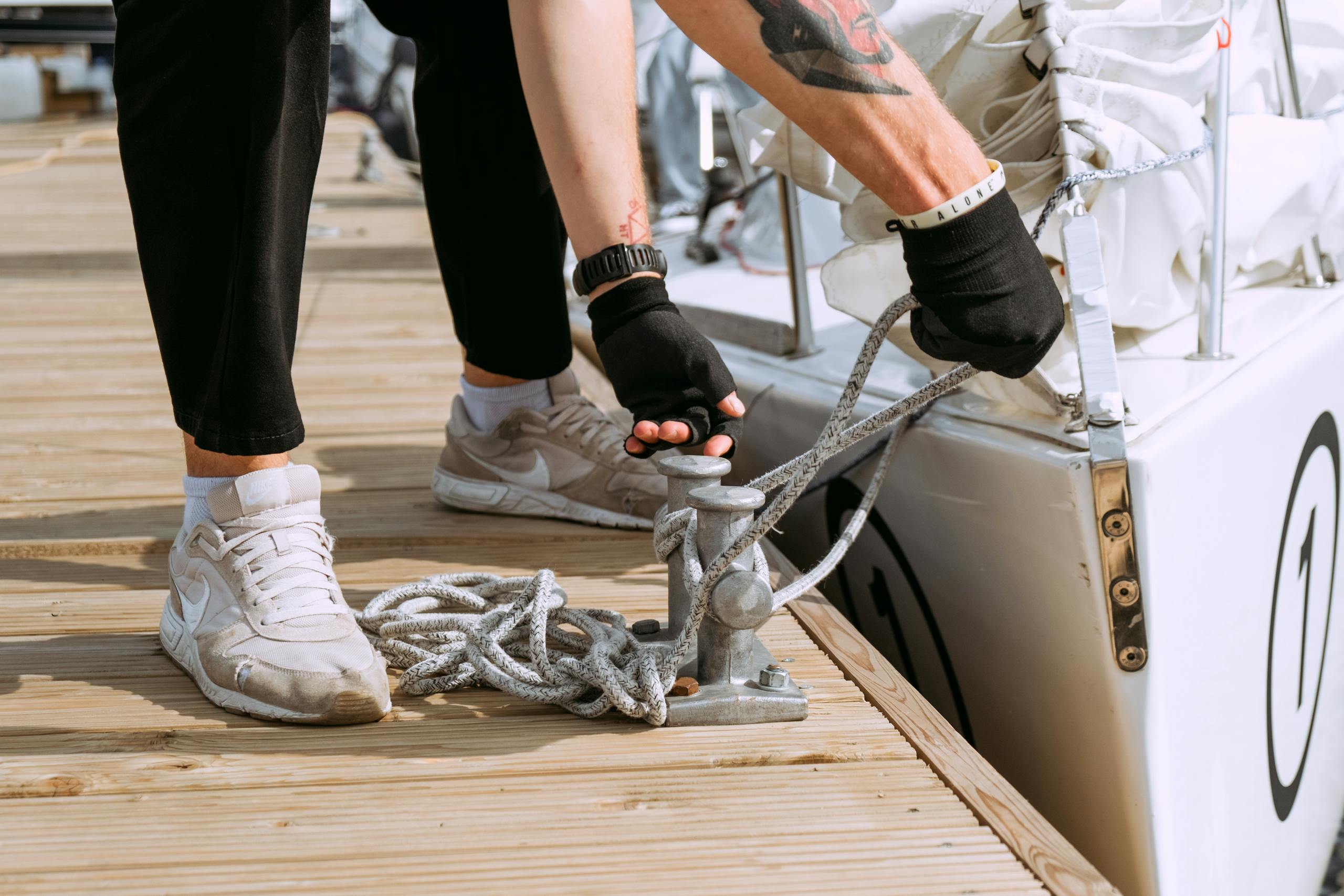 Close-up of a sailor tying a yacht to the dock using mooring rope. Nautical activity outdoors.